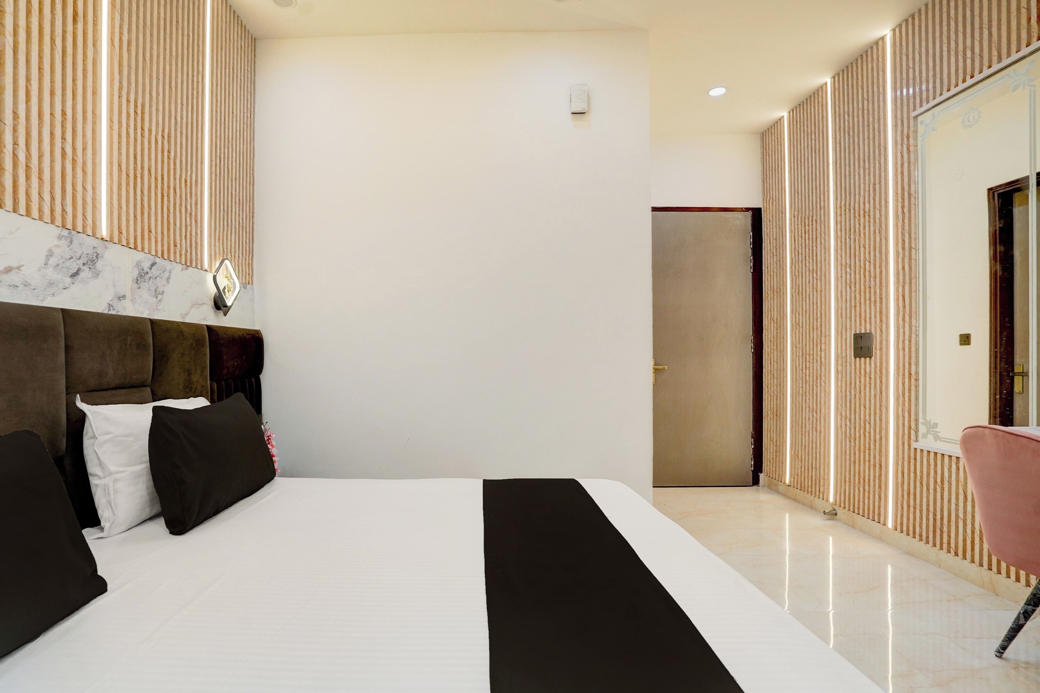Habitació d'hotel moderna amb un llit gran, un capçal de llit, una tauleta de nit, un mirall i una porta.