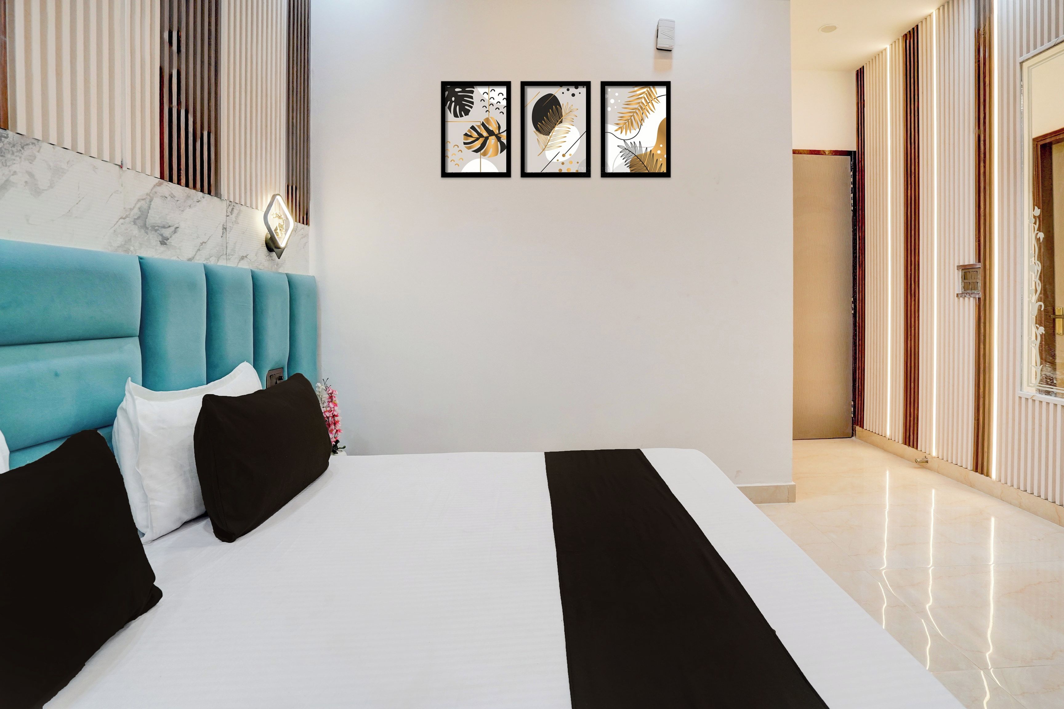 A hotel room with a bed, a blue headboard, a marble wall, and three framed artworks.