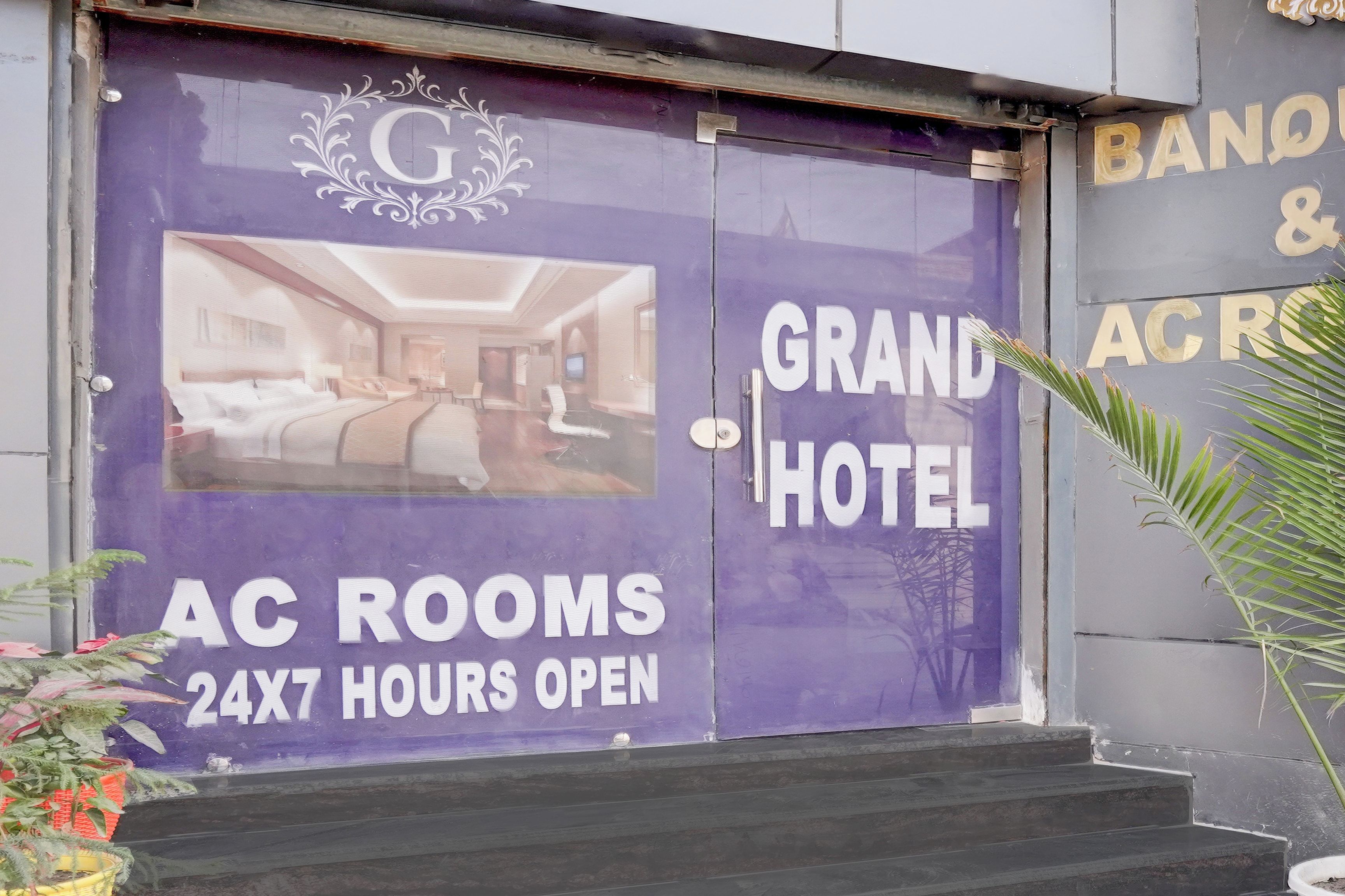 A hotel entrance with a large sign advertising 'Grand Hotel' and 'AC Rooms 24x7 Hours Open'.