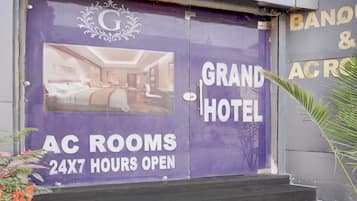 A hotel entrance with a large sign advertising 'Grand Hotel' and 'AC Rooms 24x7 Hours Open'.