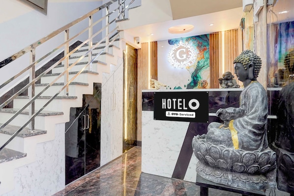 A hotel reception area with a staircase, a Buddha statue, and a sign indicating 'HOTEL OYO-Serviced'.