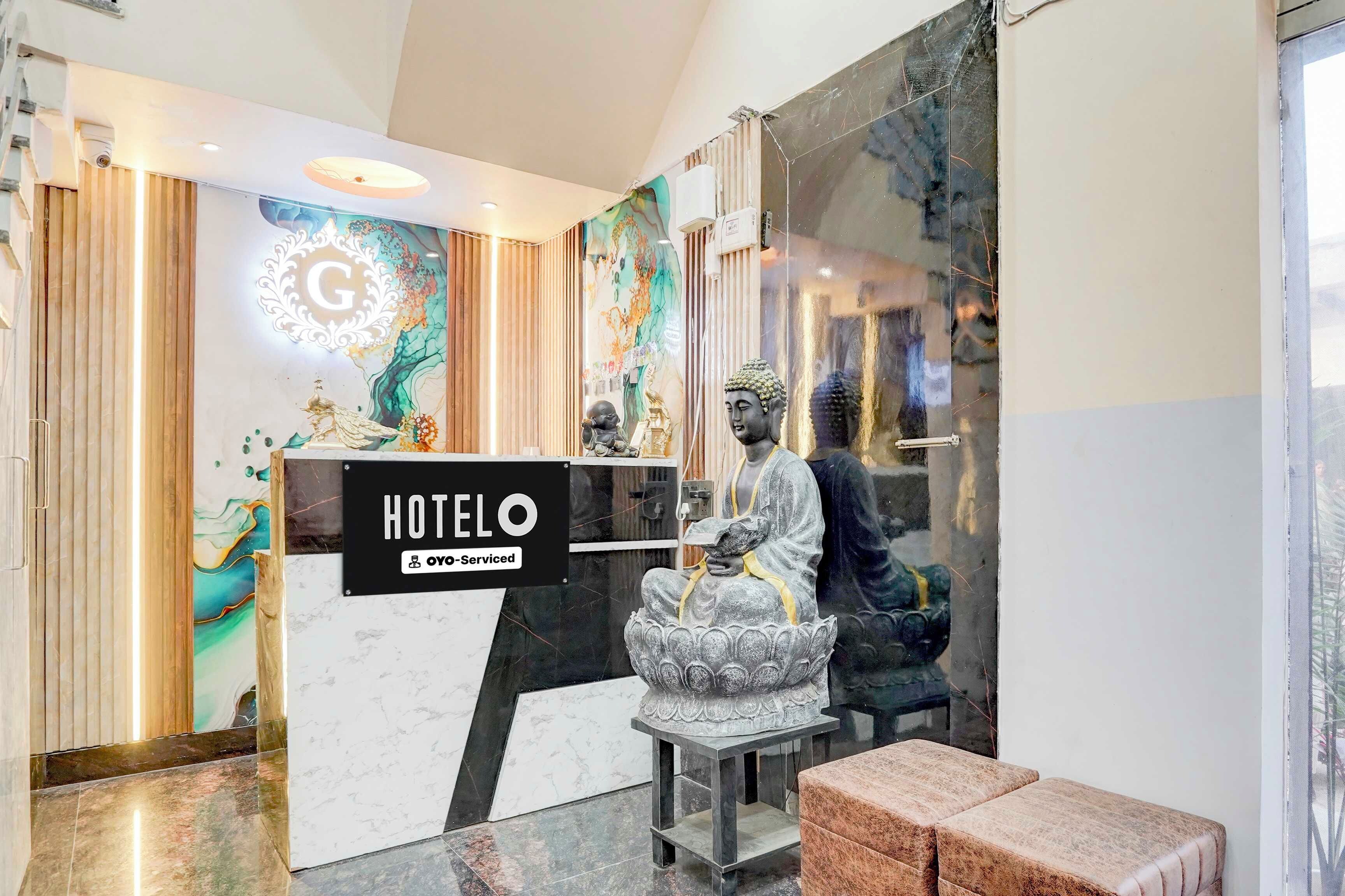 Uma área de recepção de hotel com balcão de mármore, uma estátua de Buda e uma placa indicando 'HOTEL OYO-Serviced'.