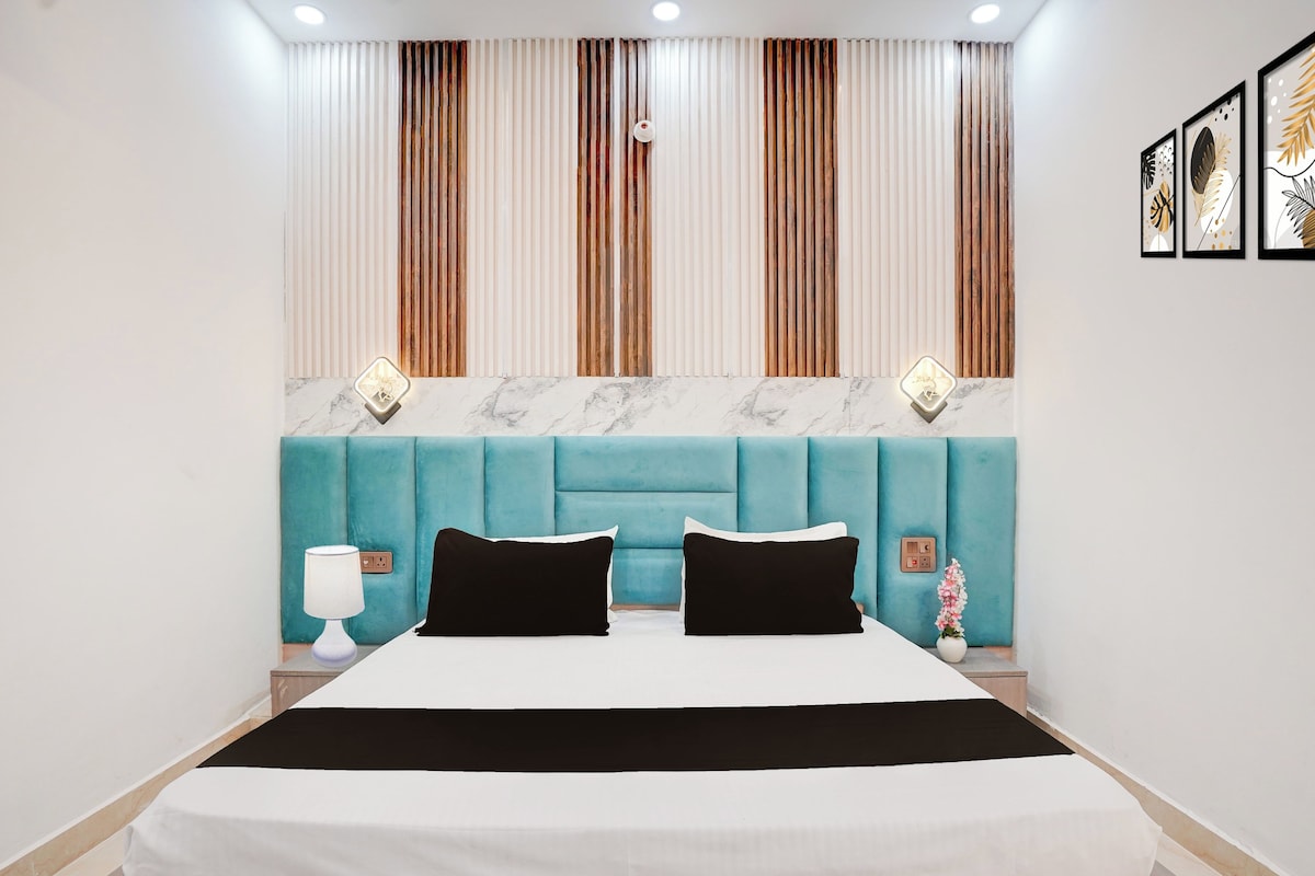 Un dormitorio moderno con un cabecero tapizado en color aguamarina, una colcha blanca y dos almohadas negras.