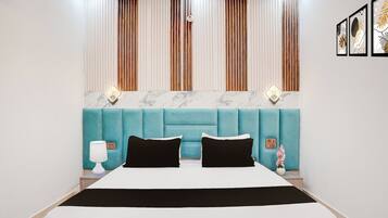 Un dormitorio moderno con un cabecero tapizado en color aguamarina, una colcha blanca y dos almohadas negras.
