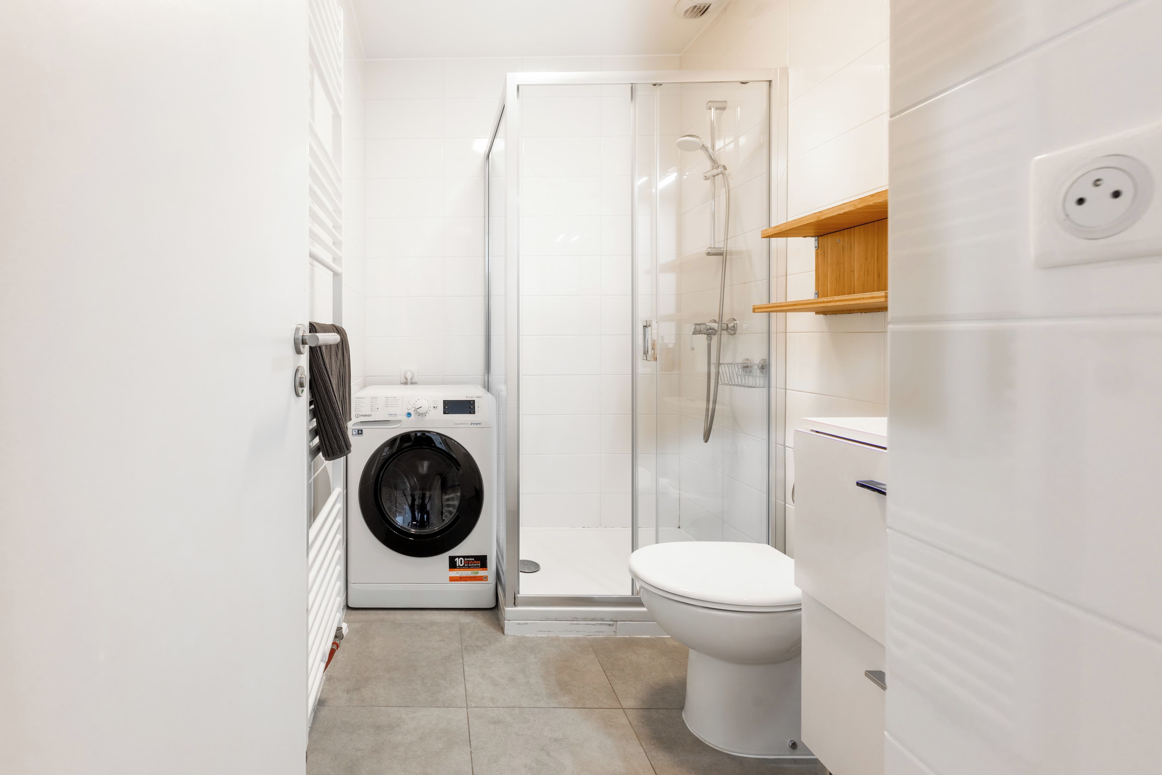 Baño compacto con lavadora, inodoro y cabina de ducha de vidrio.