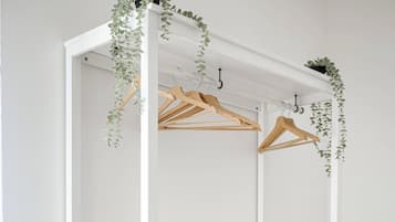 Un armario blanco con estantes, espacio para colgar ropa y un espejo, además de un enchufe.