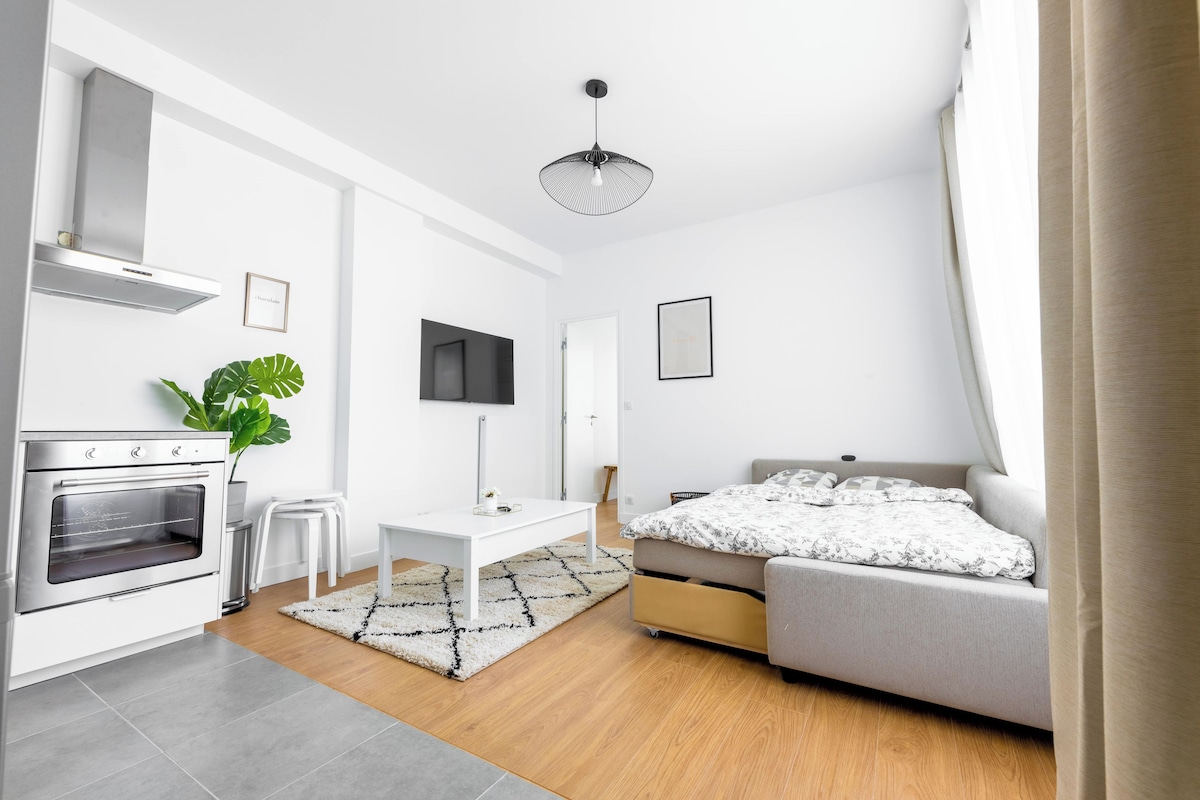 Un dormitorio moderno y bien iluminado con cama, mesita de noche y televisor montado en la pared.