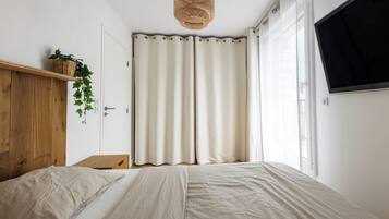 Un dormitorio con cama, cabecera de madera, televisor montado en la pared y ventana con cortinas.