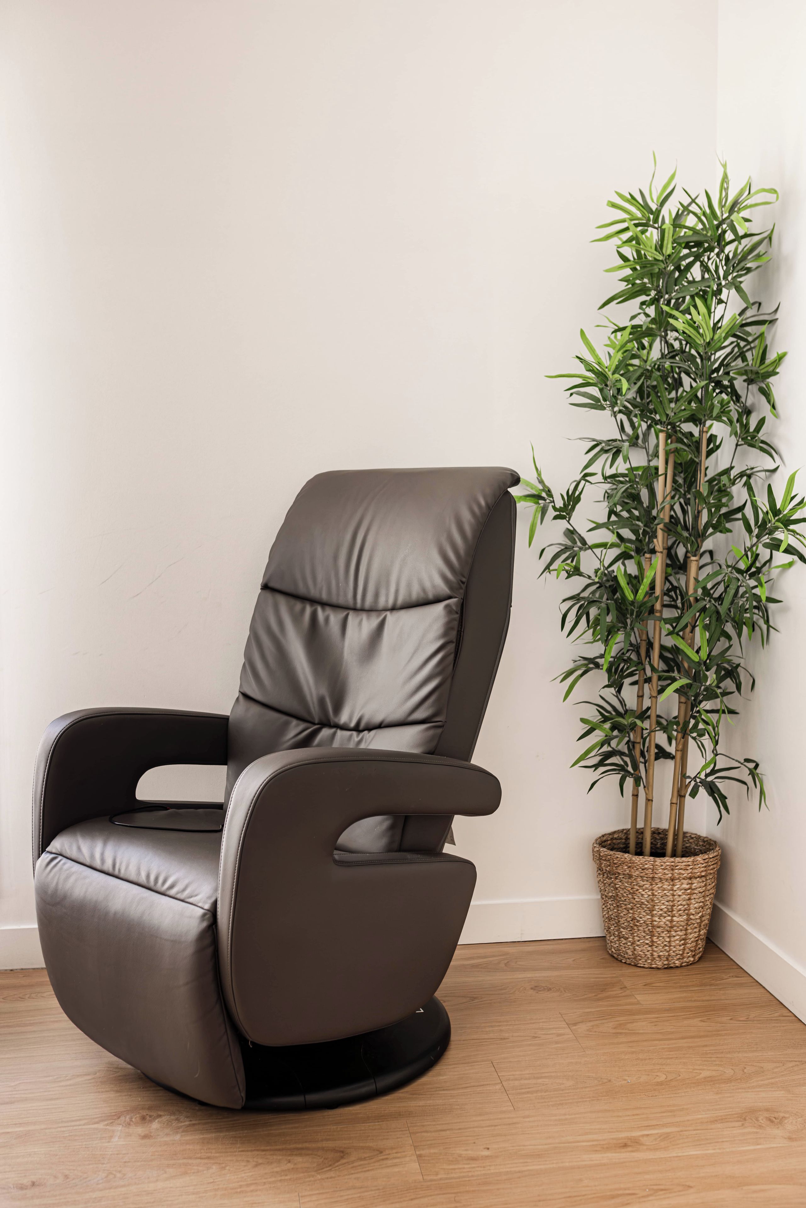 Un fauteuil inclinable en cuir foncé, doté d’un repose-pieds et accompagné d’un pot de fleurs en osier.