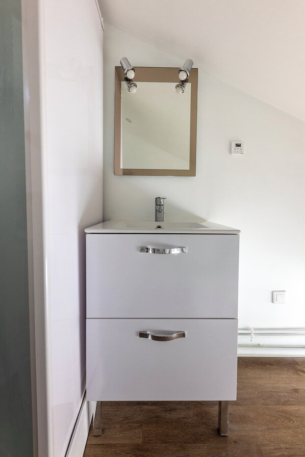 Une salle de bain avec un meuble-lavabo blanc, un miroir et un thermostat fixé au mur.