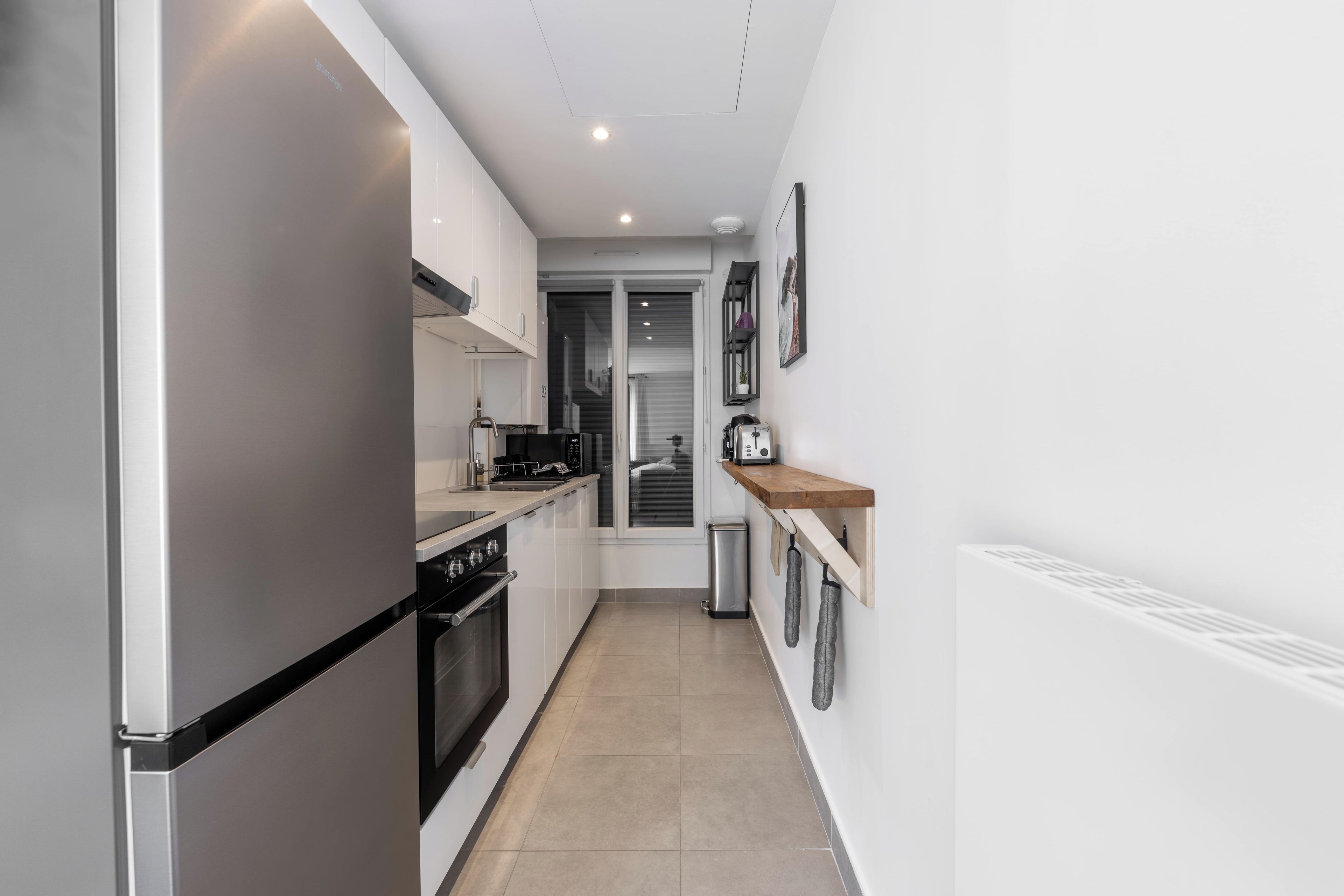 A modern kitchen with a stainless steel refrigerator, a built-in oven, and a microwave. There is a wooden countertop with a toaster and a small shelf above it.