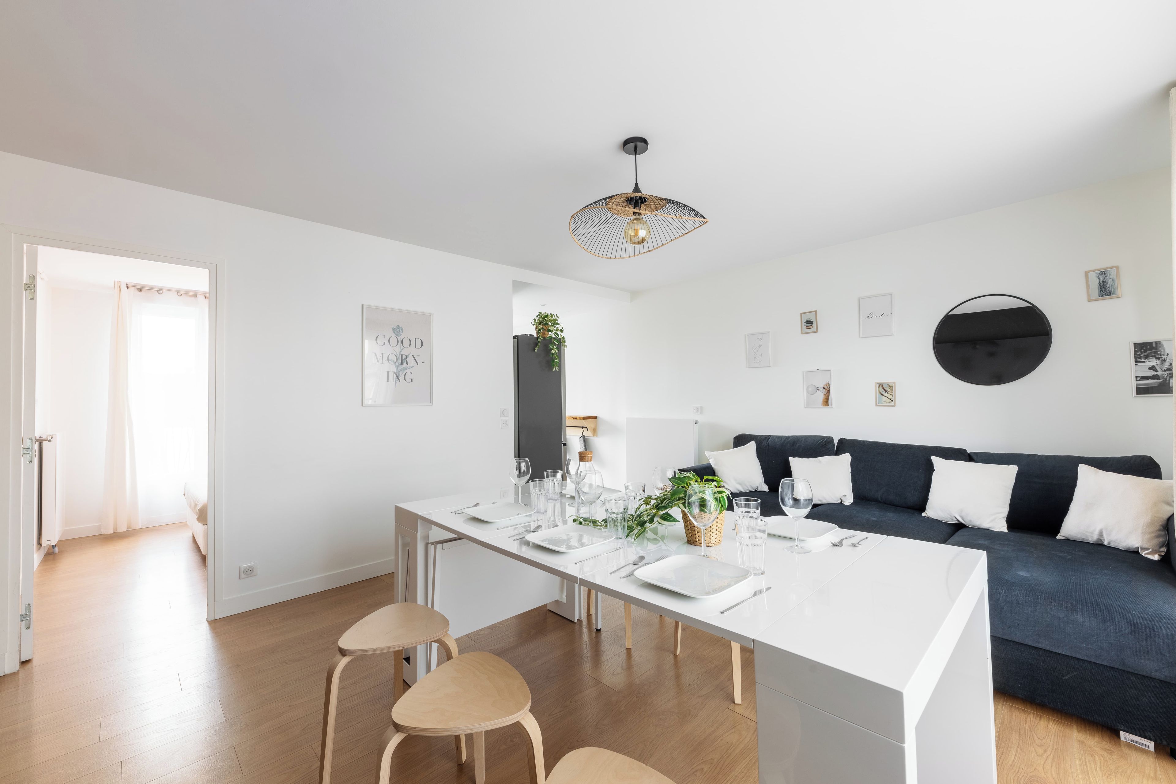Una cocina moderna con una mesa de comedor para cuatro personas, un sofá oscuro y una lámpara colgante.