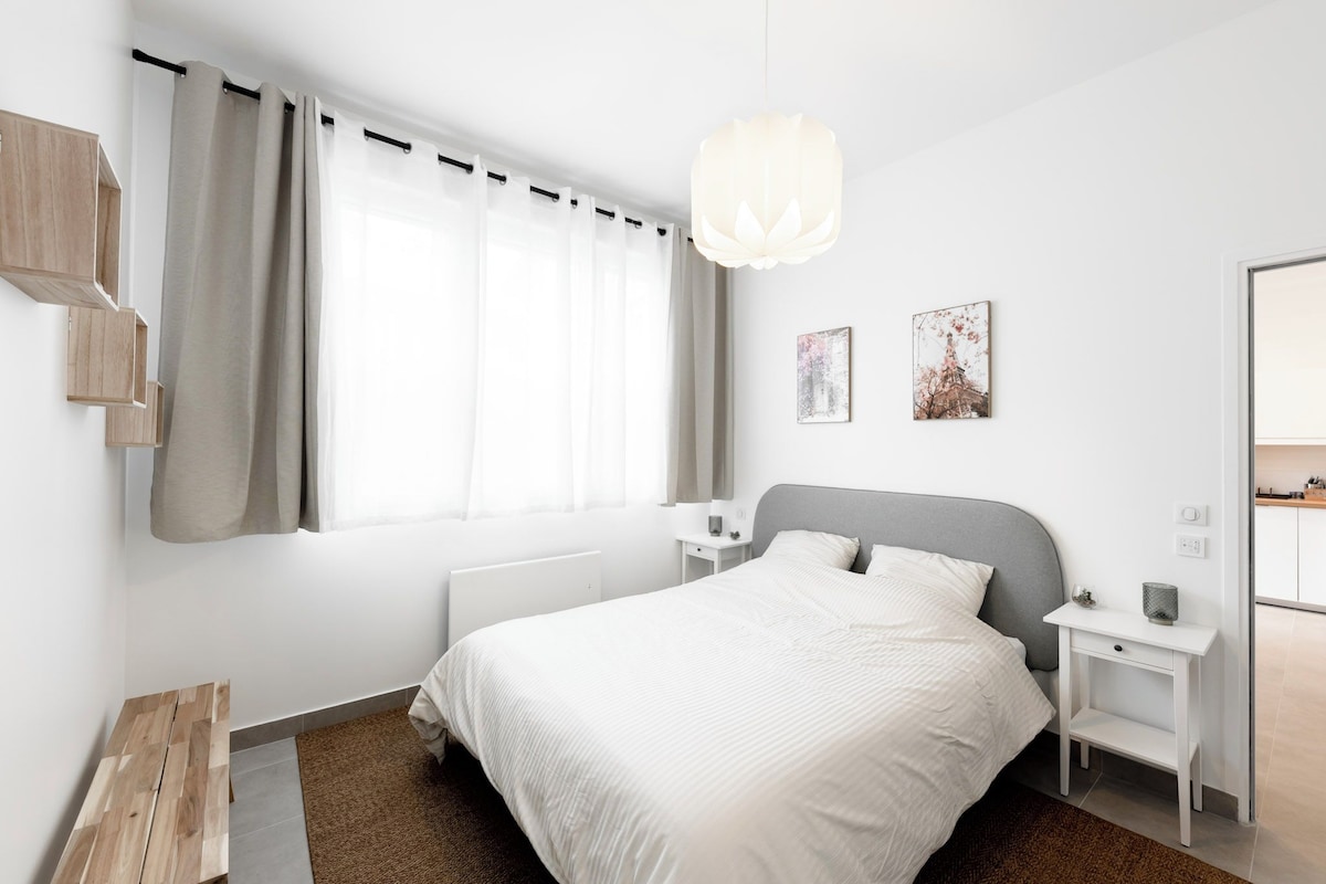 Un dormitorio moderno con una cama grande, mesitas de noche, una lámpara colgante y dos obras de arte en la pared.