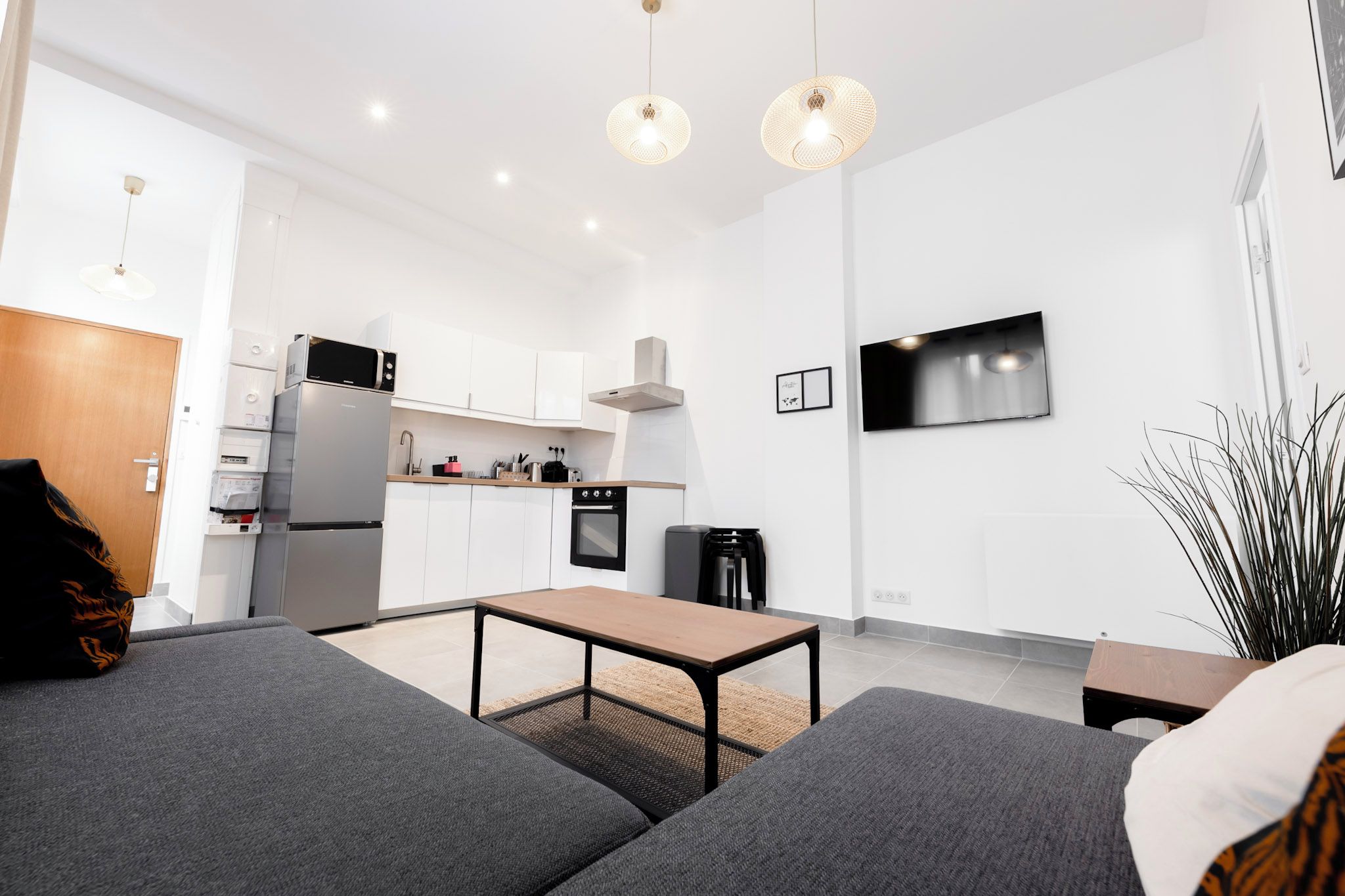 Een moderne keuken met witte kasten, een magnetron, oven en een televisie aan de muur.