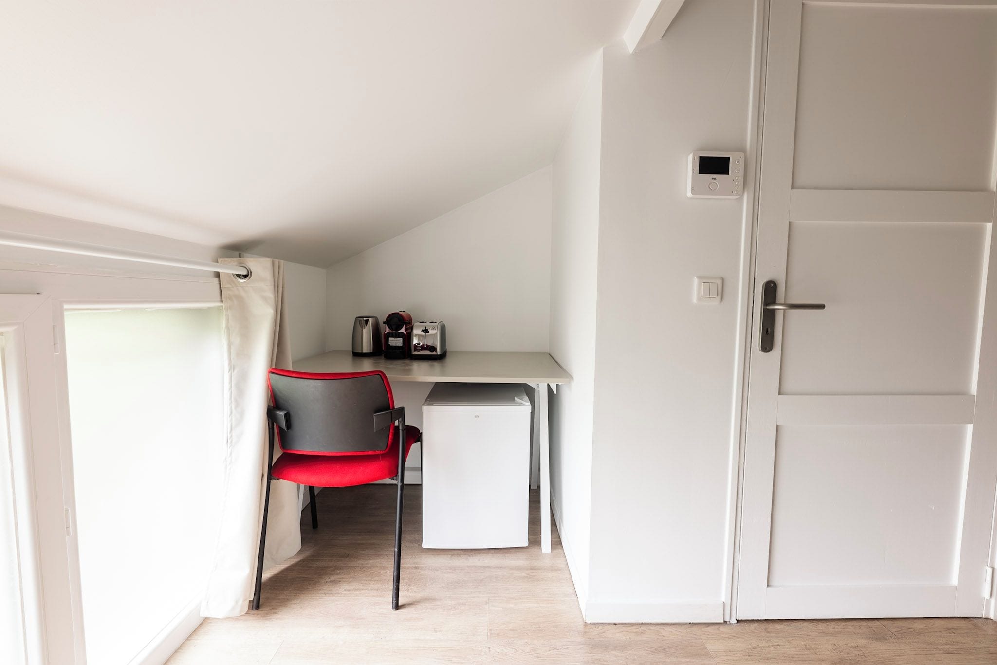 Ein kleines Zimmer mit Küchenzeile, einem Sessel, einem kleinen Kühlschrank und einer Tür mit Lichtschalter.
