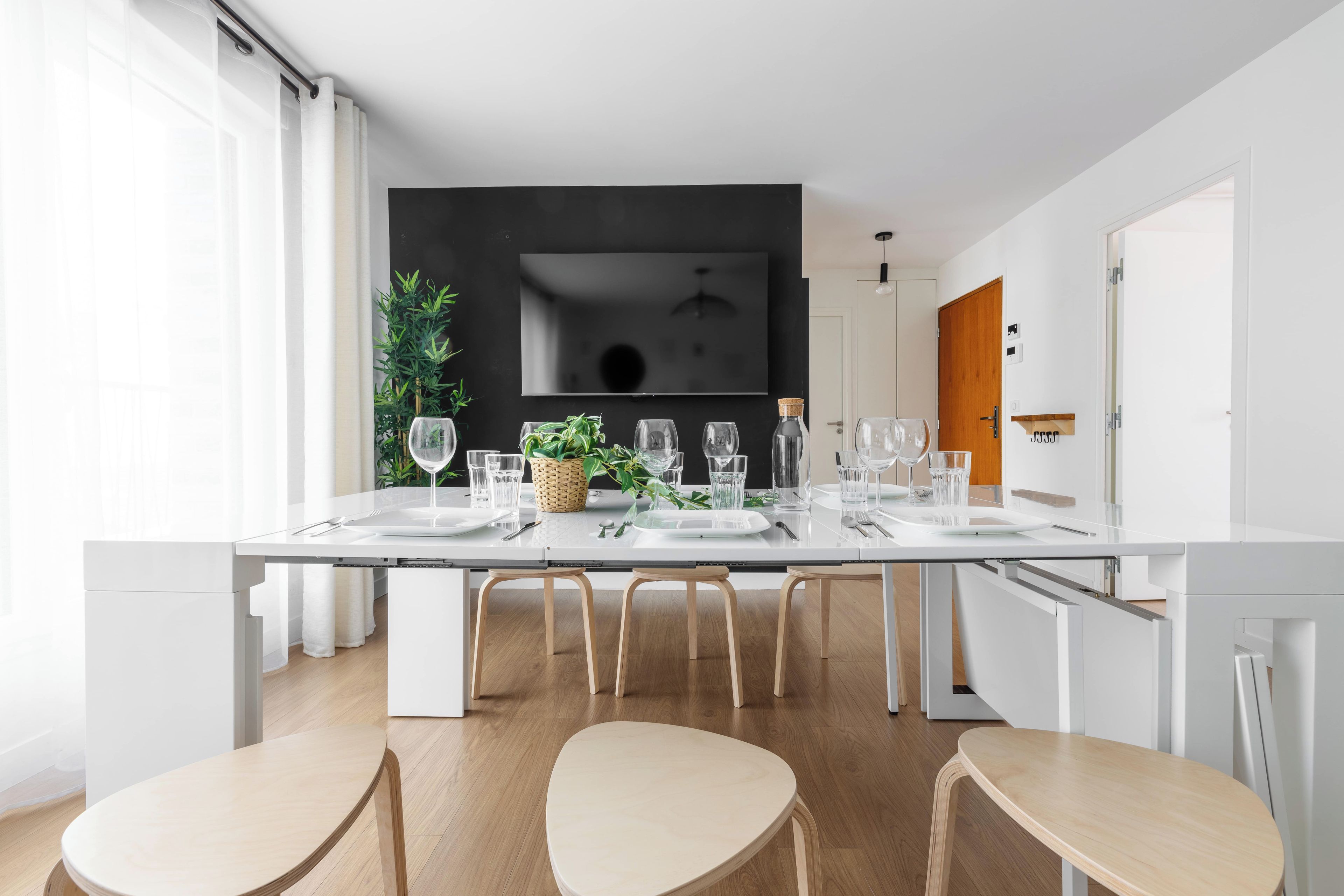 Una cocina moderna con una mesa de comedor para cuatro personas, sillas de madera y un televisor negro grande montado en la pared.