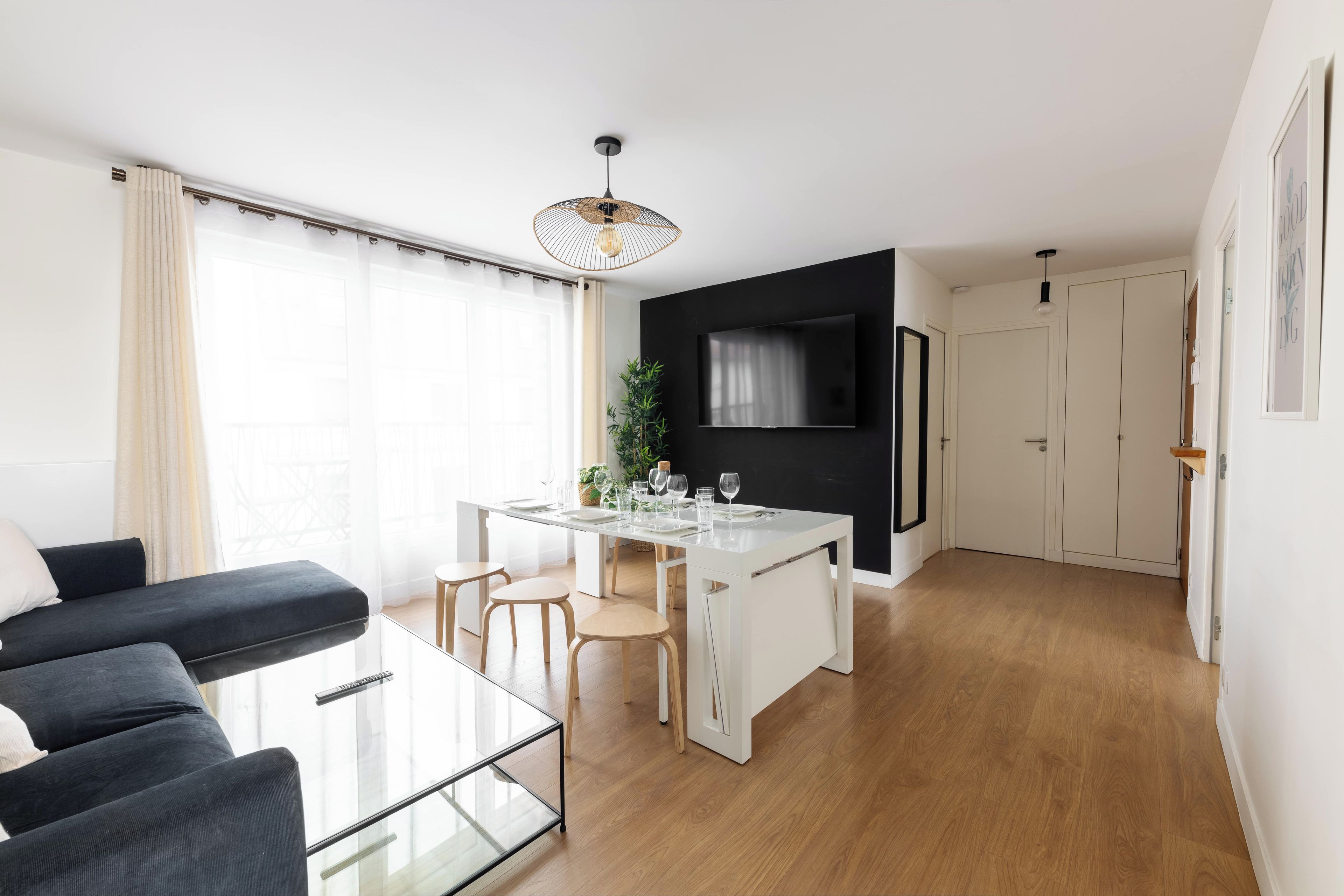 Een moderne woonruimte met een glazen eettafel, een zwarte bank en een televisie aan een zwarte muur.