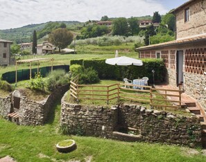 Un patio con paredes de piedra, cerca de madera, un pequeño jardín y una mesa con sombrilla blanca.