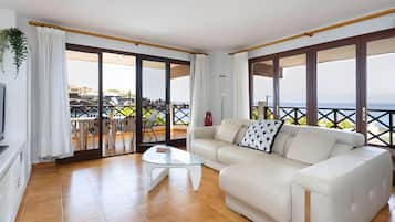 A living room with a sofa, a glass coffee table, and a view of the sea through large windows.