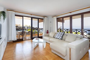 A living room with a sofa, a glass coffee table, and a view of the sea through large windows. - Apartment 'Neptuno Ocean Experience By Sydney' with Sea View, Shared Pool and Wi-Fi (La Arena)