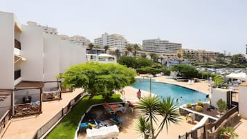 A pool area with lounge chairs, a tree, and a view of surrounding buildings.