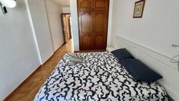 A bedroom with a bed, a nightstand, a wooden wardrobe, and a framed picture on the wall.