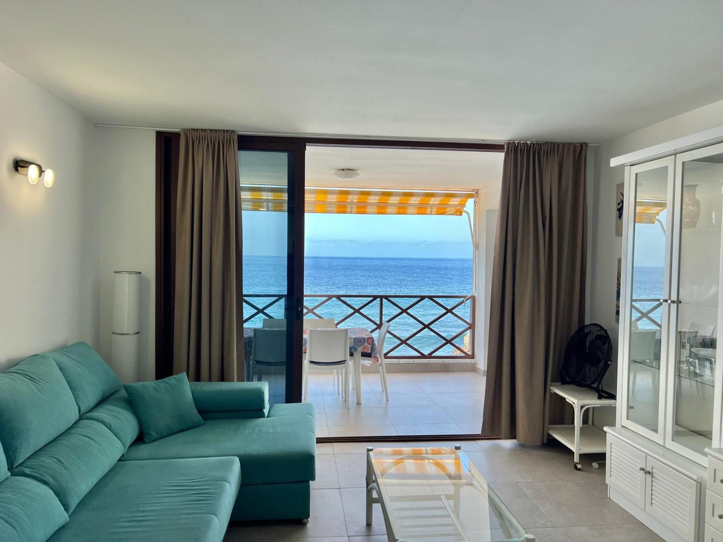 Una habitación con un sofá color turquesa, una mesa de vidrio y vista al mar desde un balcón.
