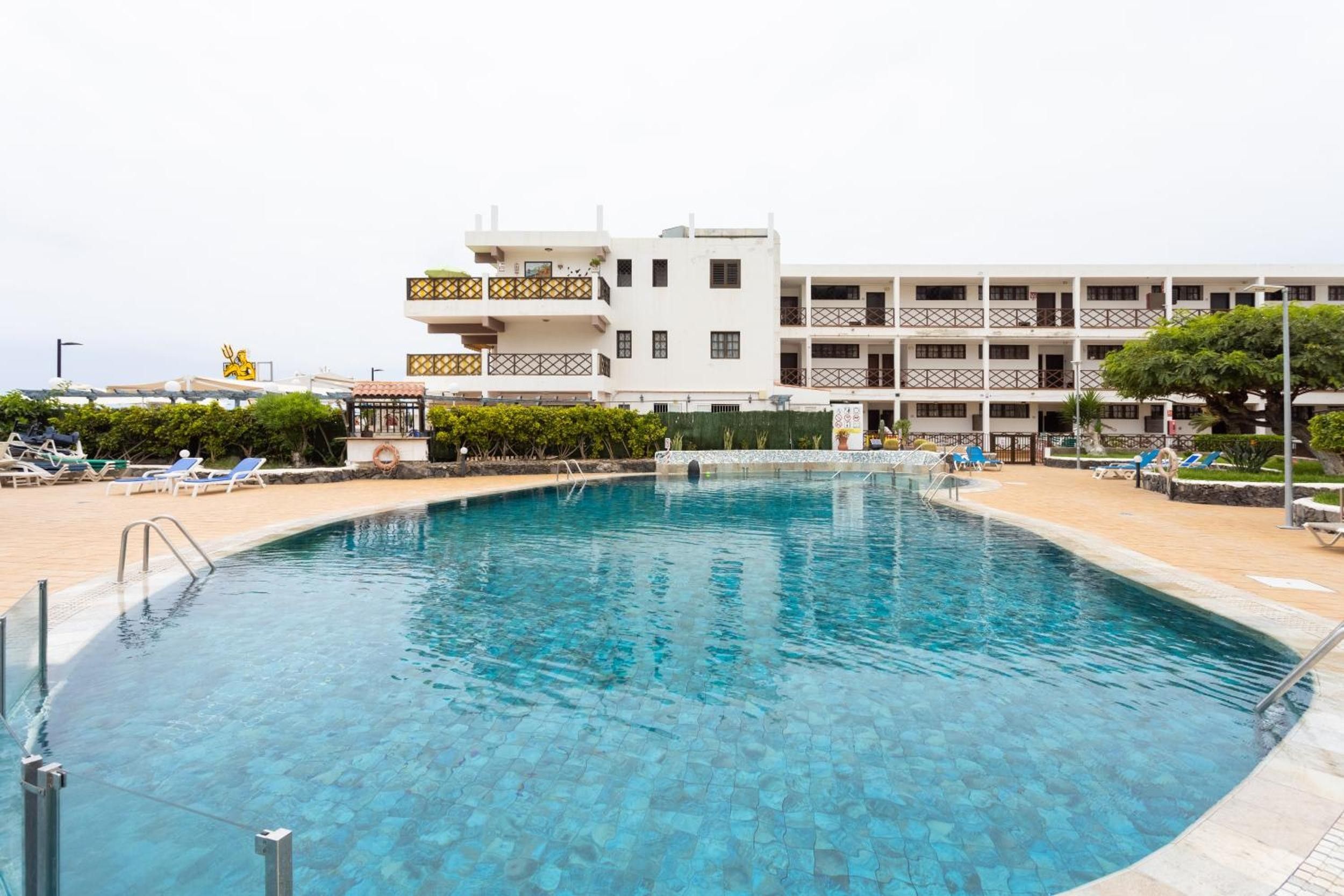 A swimming pool with clear blue water, surrounded by lounge chairs and a building with multiple balconies.