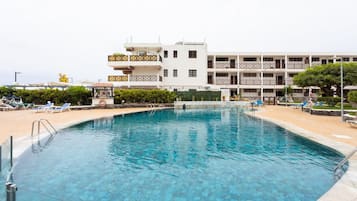 A swimming pool with clear blue water, surrounded by lounge chairs and a building with multiple balconies.