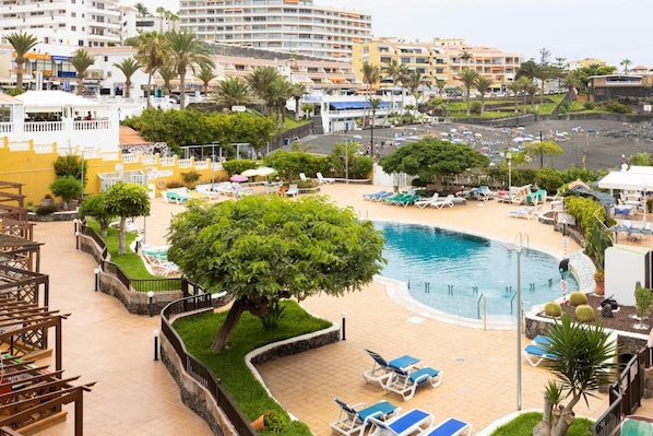 A resort with a swimming pool, lounge chairs, and a view of the beach.