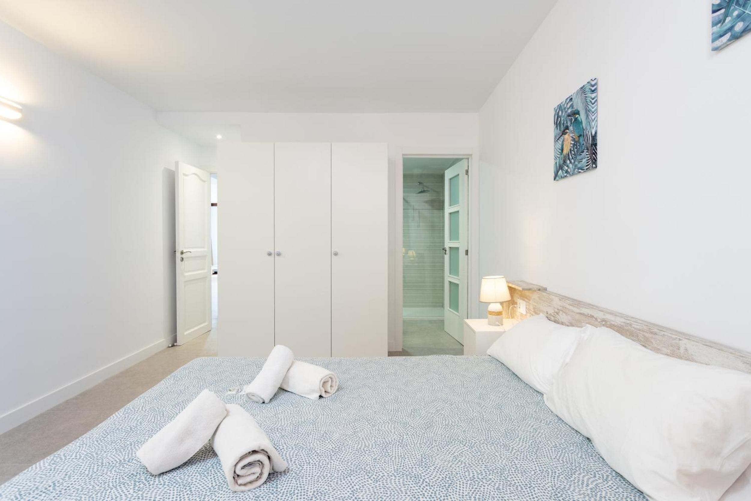 A hotel room with a bed, a nightstand, a lamp, a door leading to a bathroom, and a wall with a picture.