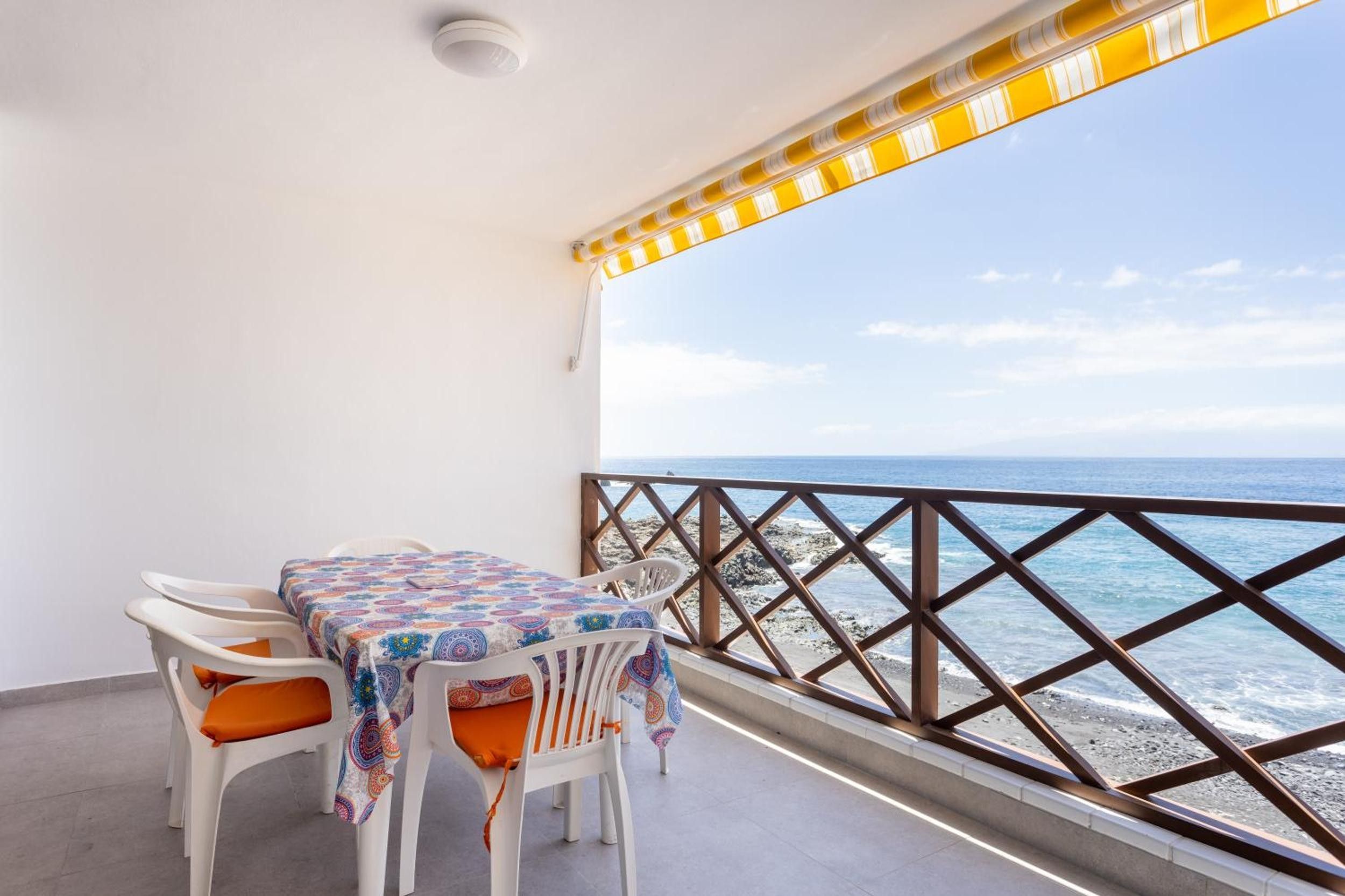 A balcony with a table and chairs, overlooking the sea.