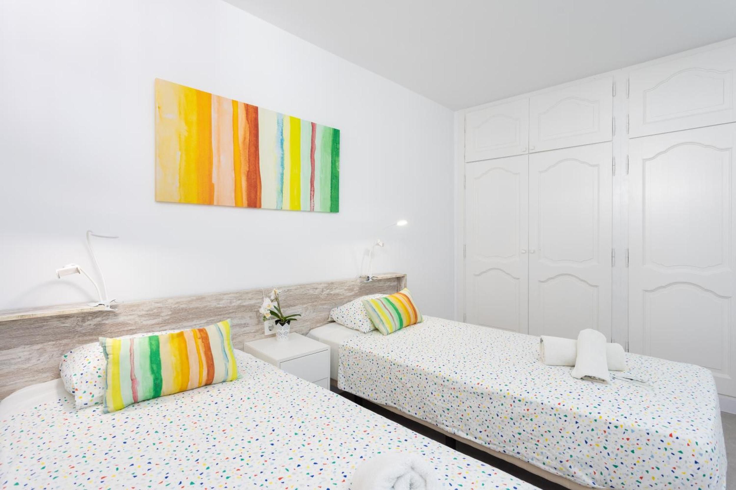 A hotel room with two beds, a white wardrobe, and a colorful abstract painting on the wall.