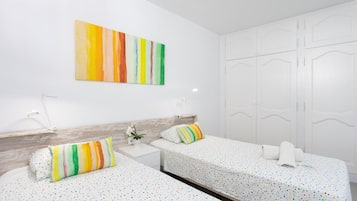 A hotel room with two beds, a white wardrobe, and a colorful abstract painting on the wall.