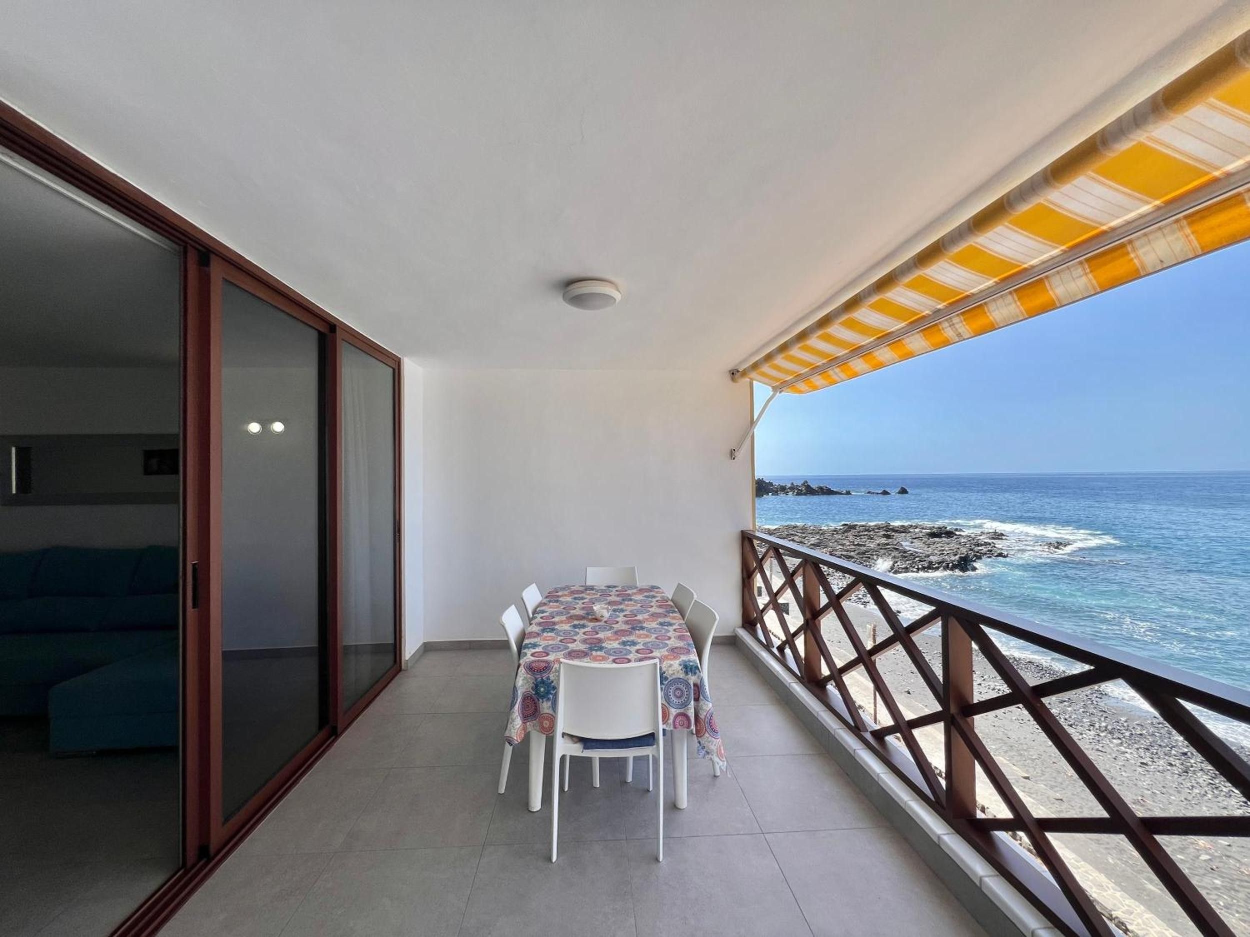 Un balcón con mesa y sillas, vista al mar y barandilla.