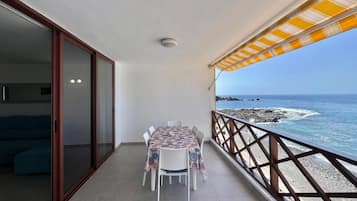 Een balkon met een tafel en stoelen, uitzicht op zee en een hekwerk.