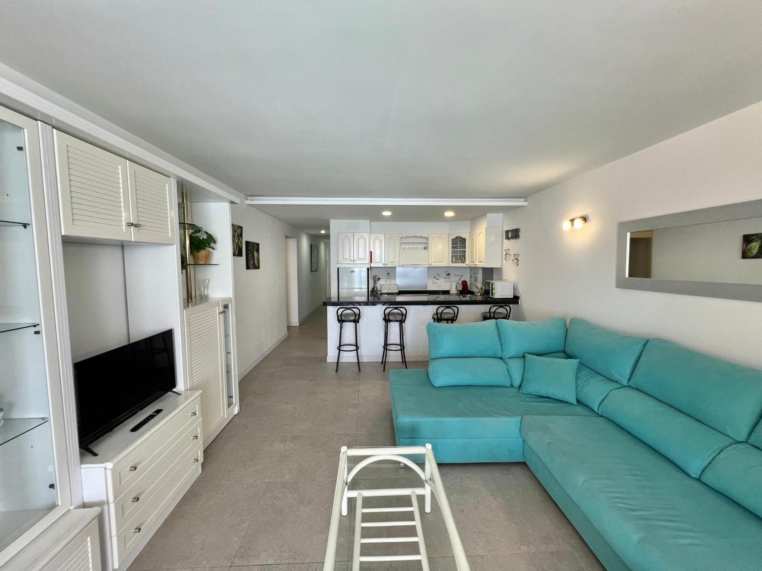 A compact living space with a kitchenette, a sofa, a TV, and a ladder.
