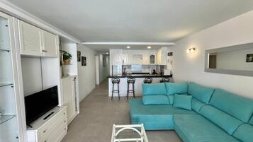 A compact living space with a kitchenette, a sofa, a TV, and a ladder.