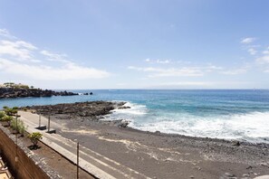 A coastal road with rocky terrain leading to the sea, a clear sky, and distant buildings. - Vacation Apartment 'Playa De La Arena By Sydney' with Sea View, Shared Pool and Wi-Fi (Santa Cruz de Tenerife)