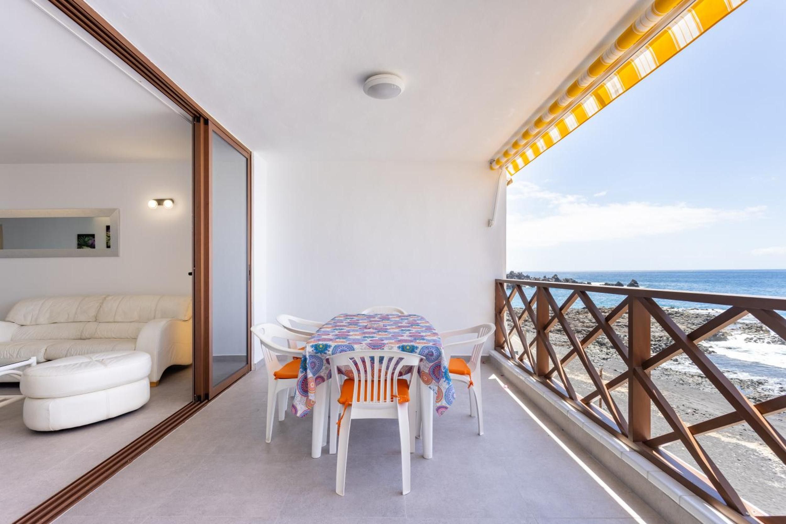 A balcony with a table and chairs, a sofa, and a view of the sea.