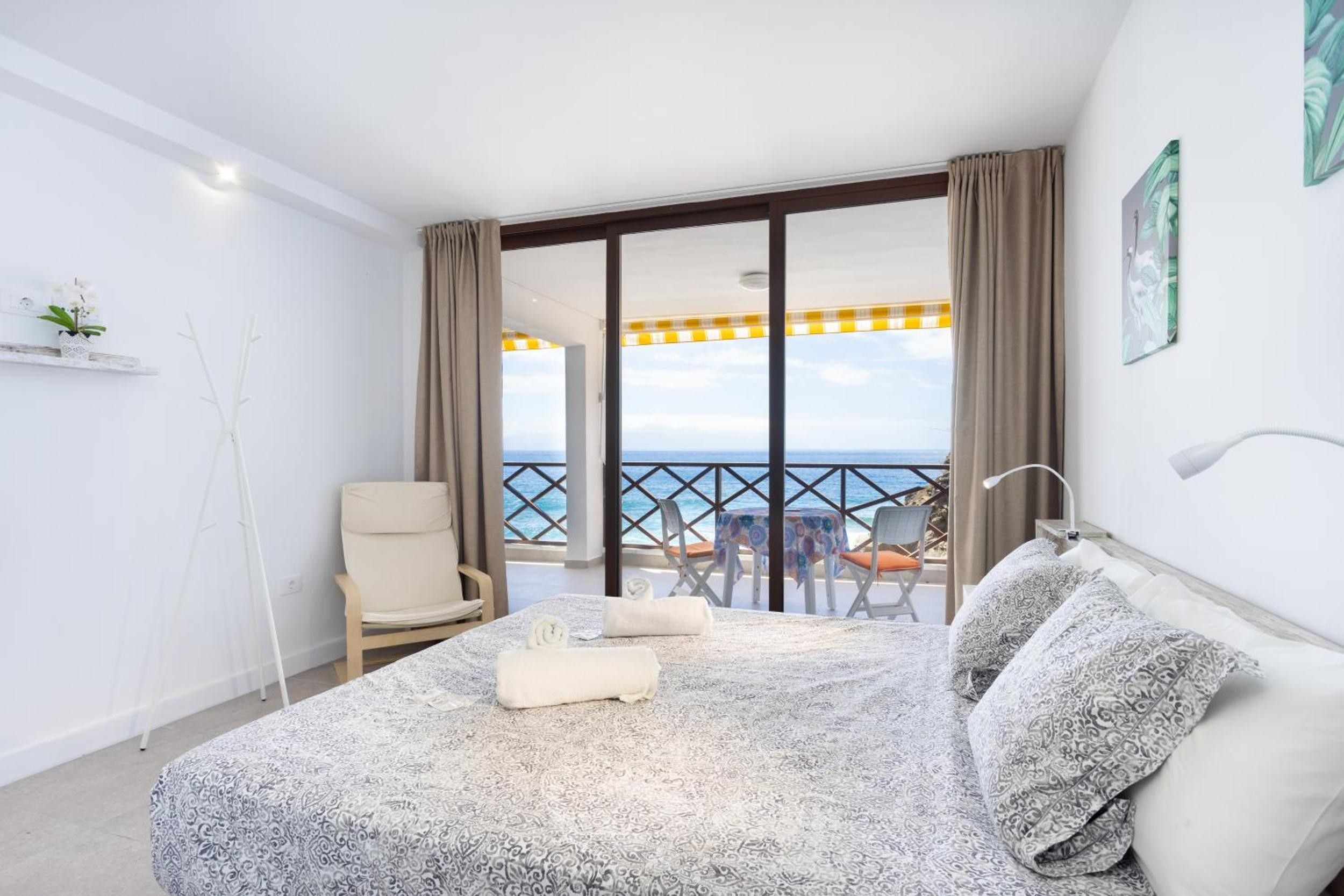 Een hotelkamer met een bed, een stoel, een tafel en uitzicht op zee.