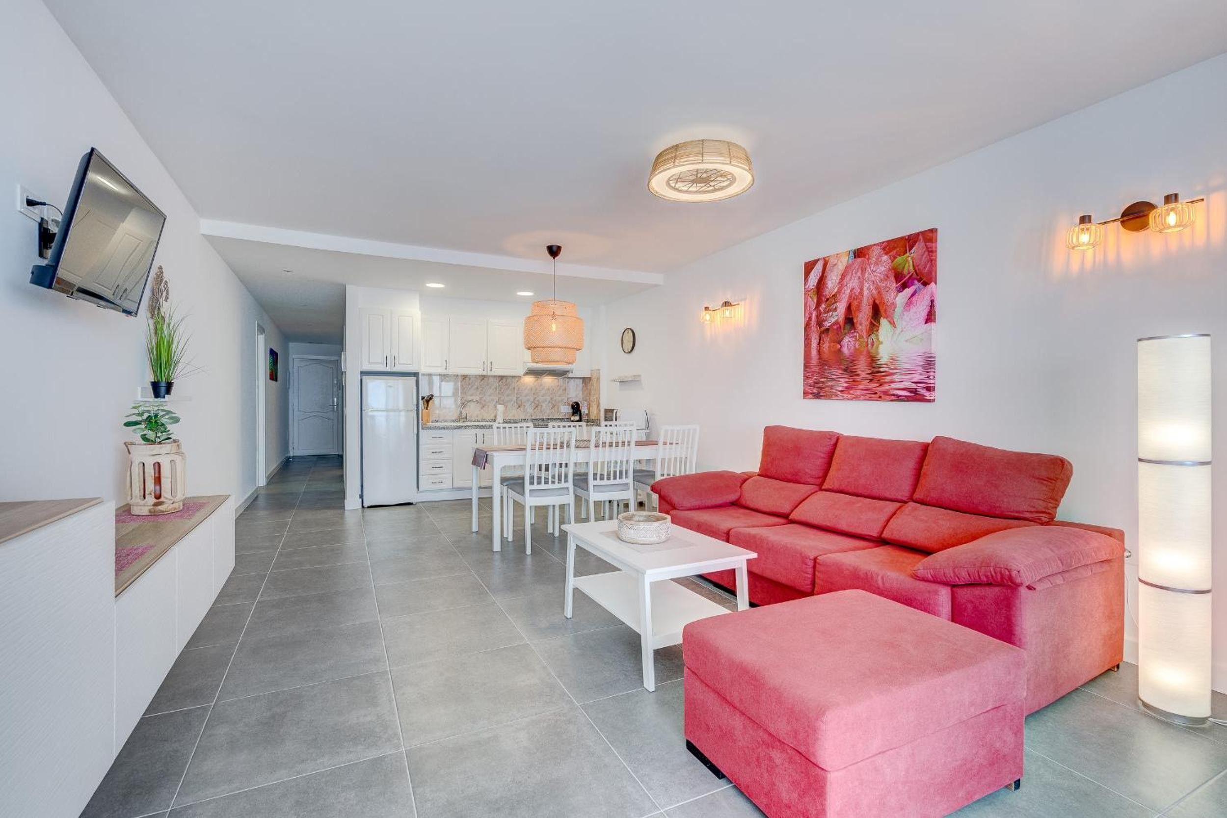 Een moderne leefruimte met een rode bank, een witte eettafel en een keuken op de achtergrond.
