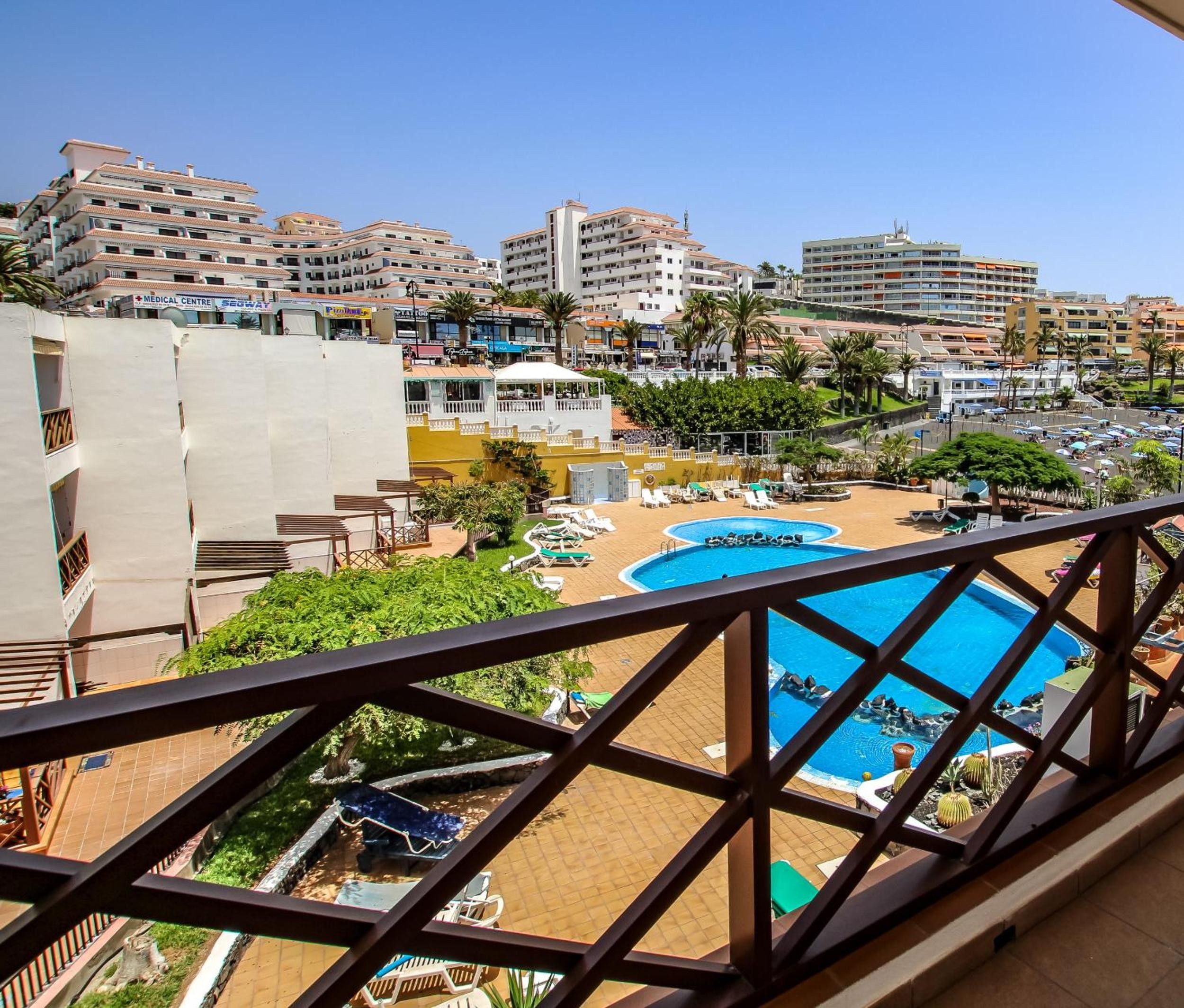 A resort with a large swimming pool, multiple lounge areas, and a view of surrounding buildings.