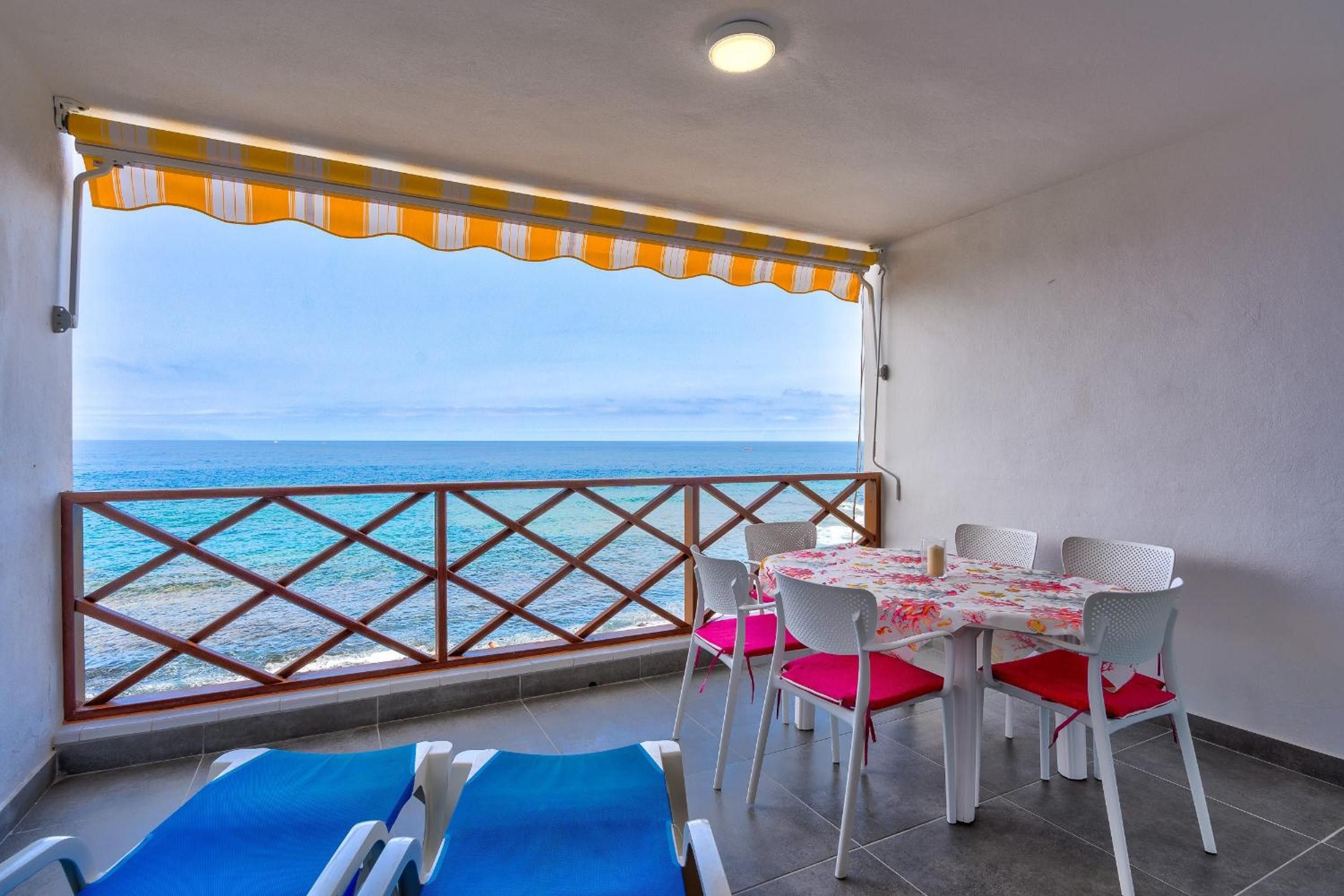 A balcony with a view of the sea, a table with chairs, and two sun loungers.