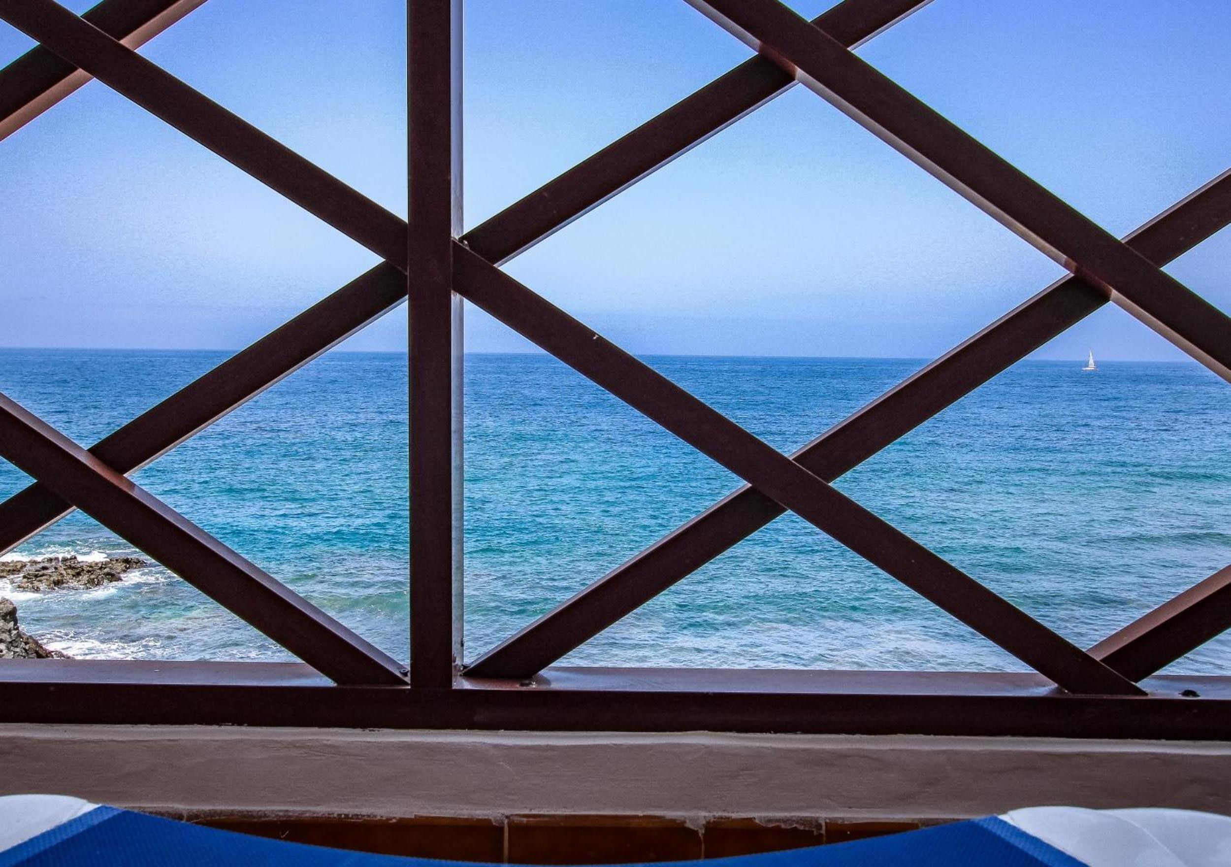 A view through a metal lattice structure with the ocean and a sailboat in the distance.
