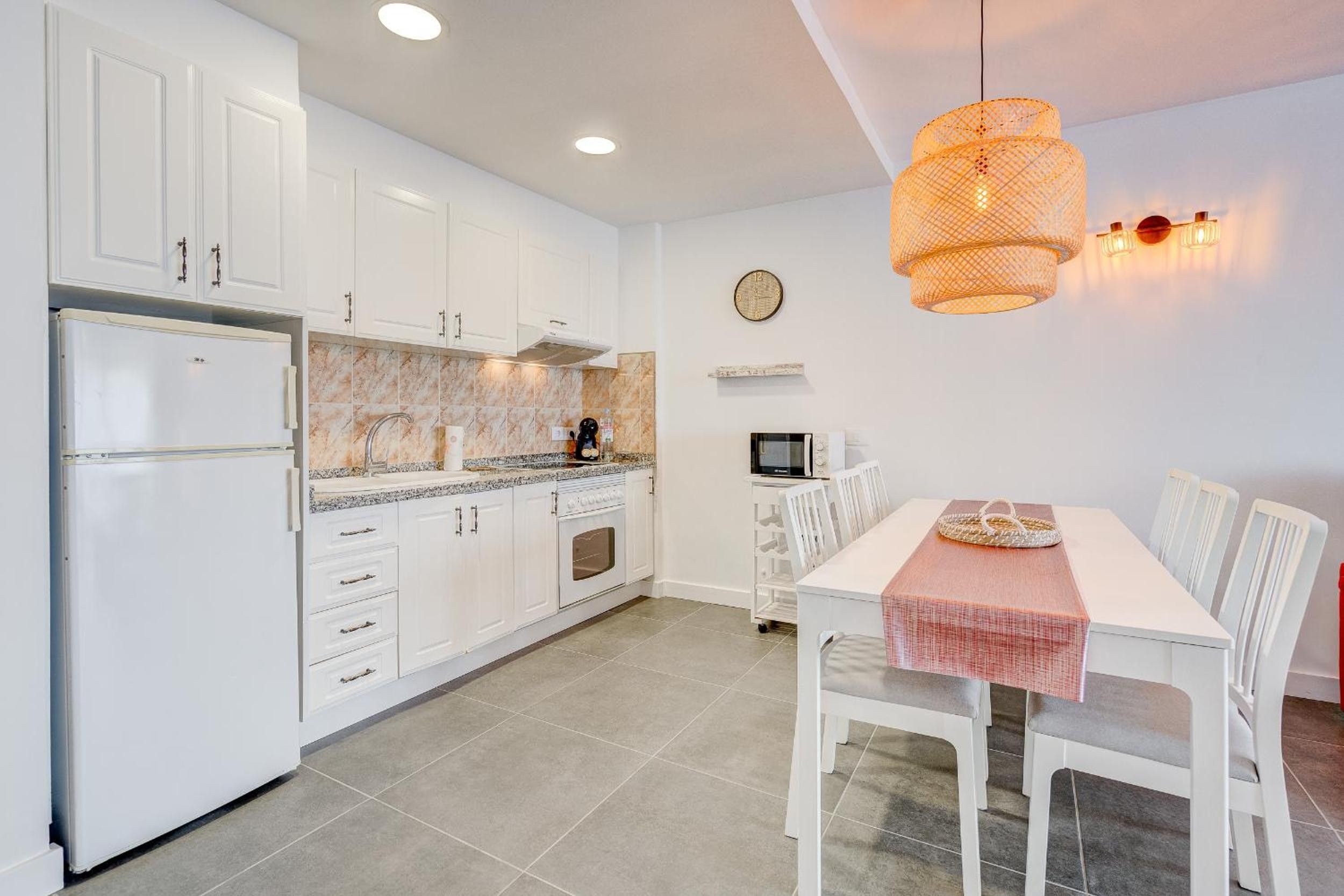 A modern kitchen with white cabinets, a built-in oven, and a dining area with a table and chairs.