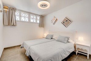 A bedroom with two beds, a window with curtains, a bedside table with a lamp, and a wall-mounted light fixture. - Vacation Apartment 'Neptuno 2a017' with Sea View, Shared Pool and Wi-Fi (Santa Cruz de Tenerife)