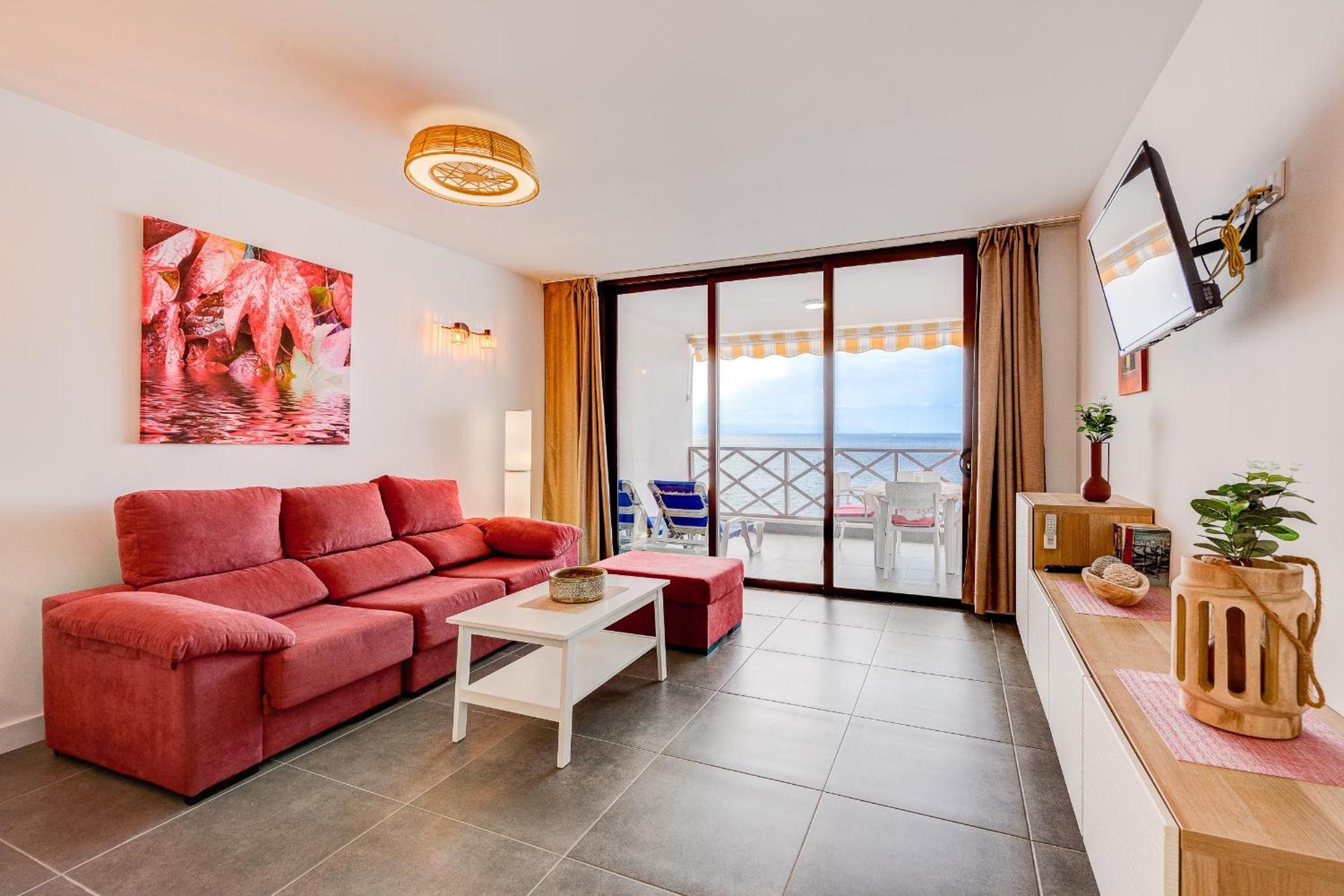 A living room with a red sofa, a white coffee table, and a large window with a view of the sea.