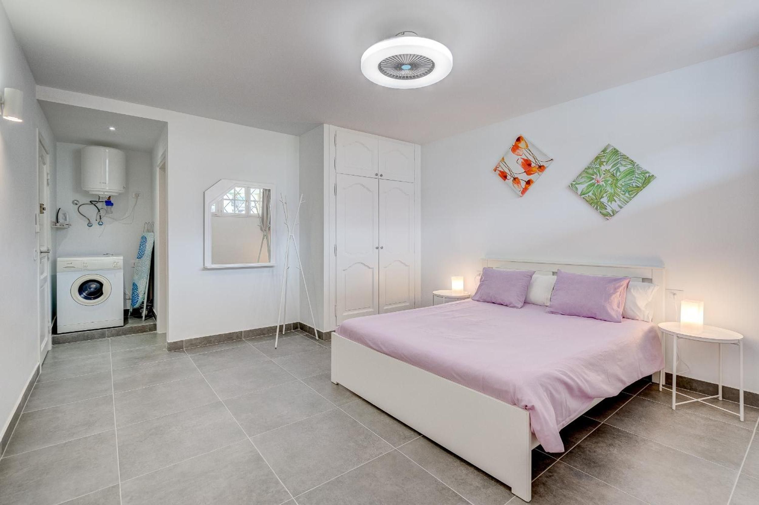 Un dormitorio con cama, mesitas de noche, lavadora y espejo.