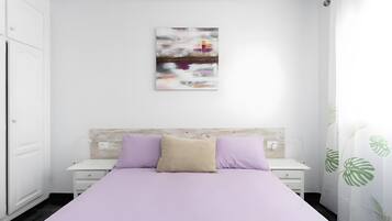 A bedroom with a bed, a nightstand, a wall-mounted artwork, and a plant.